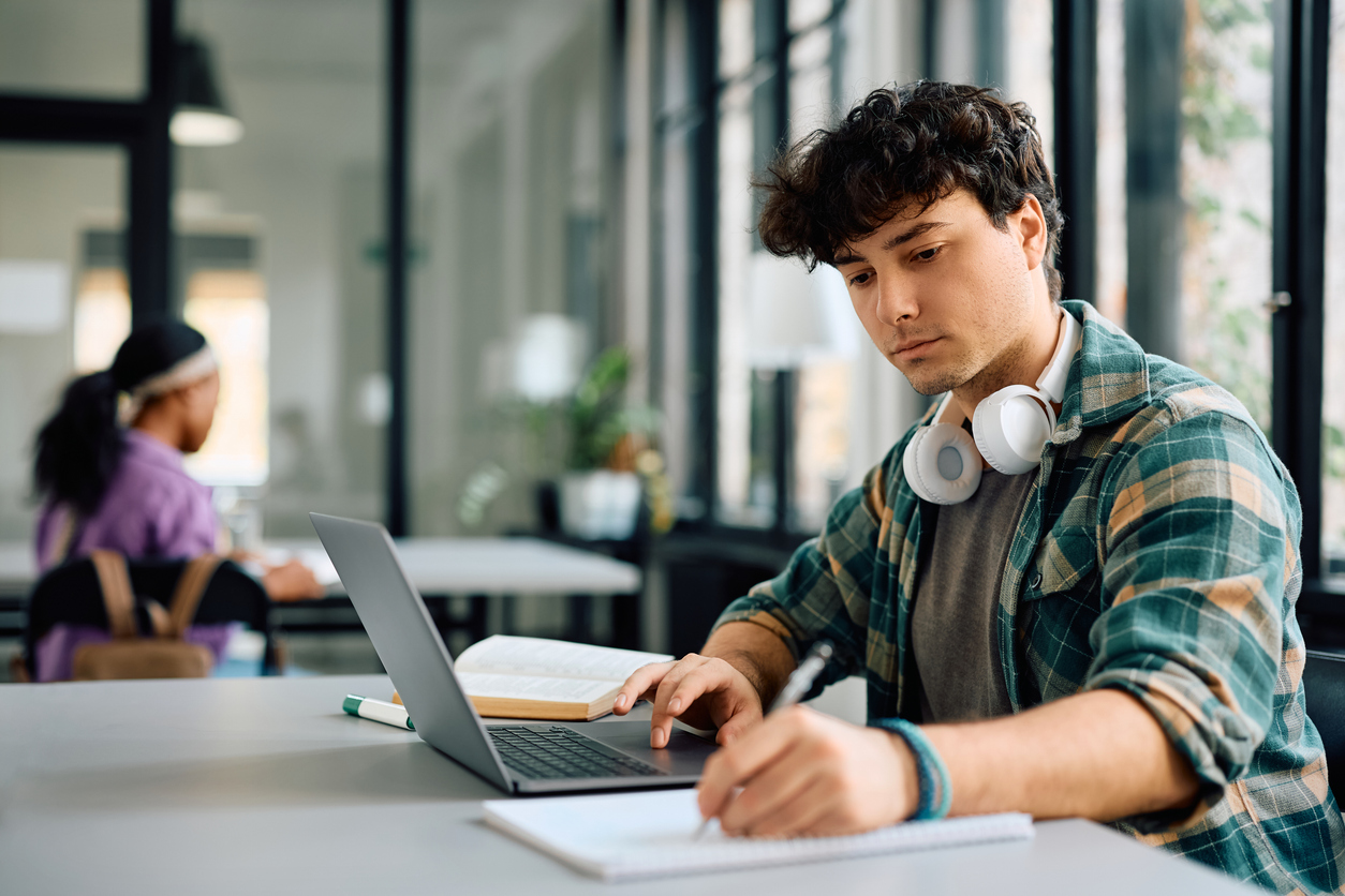 jongvolwassen jongen die leert met laptop en papier